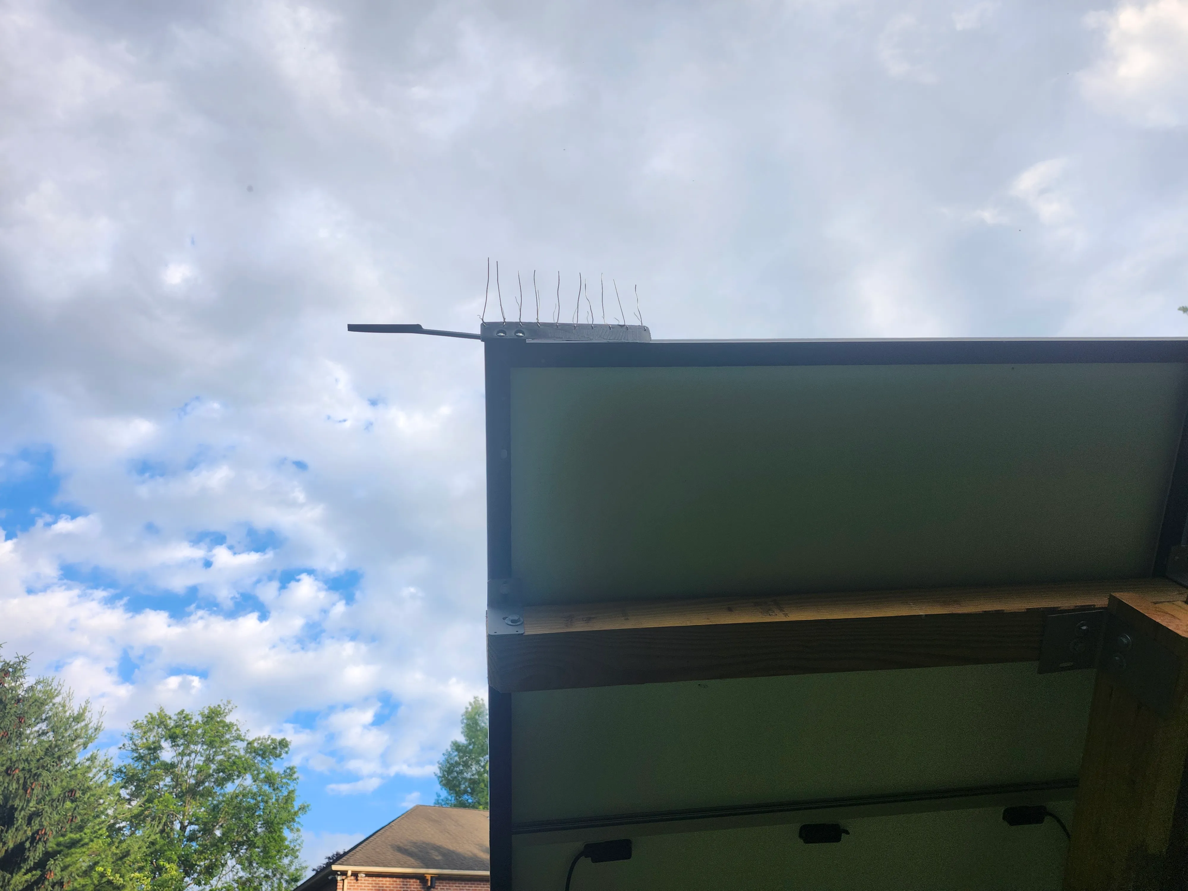 Close-up of the PerchOff corner unit mounted on a panel, with stainless spikes on top and the offset perch arm extending out